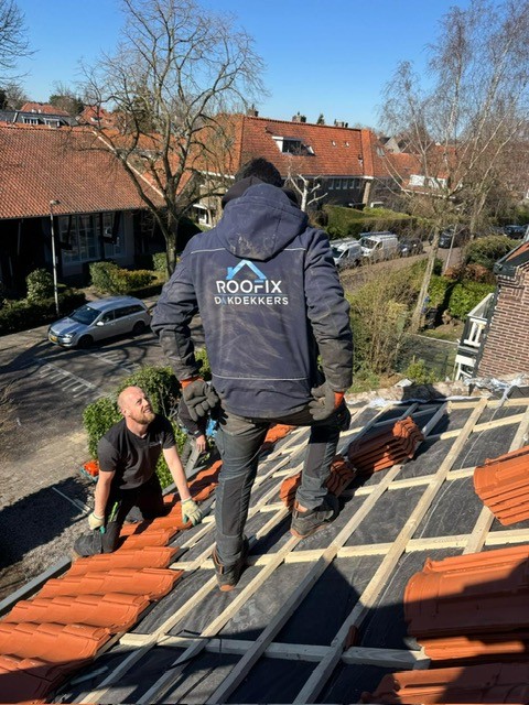 Dakdekkers van Roofix plaatsen nieuwe rode dakpannen op een schuin dak tijdens een renovatie.